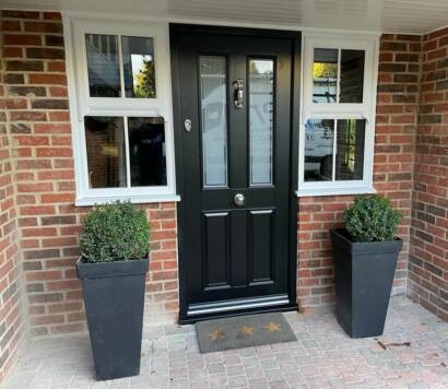 Black composite entrance door flanked by two double-pane windows on a red-brick porch